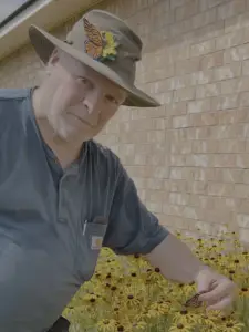 Hugh Pinckard as Monarch Butterfly Wrangler holding a Monarch Butterfly to be released on BlackEyeSusies in the background